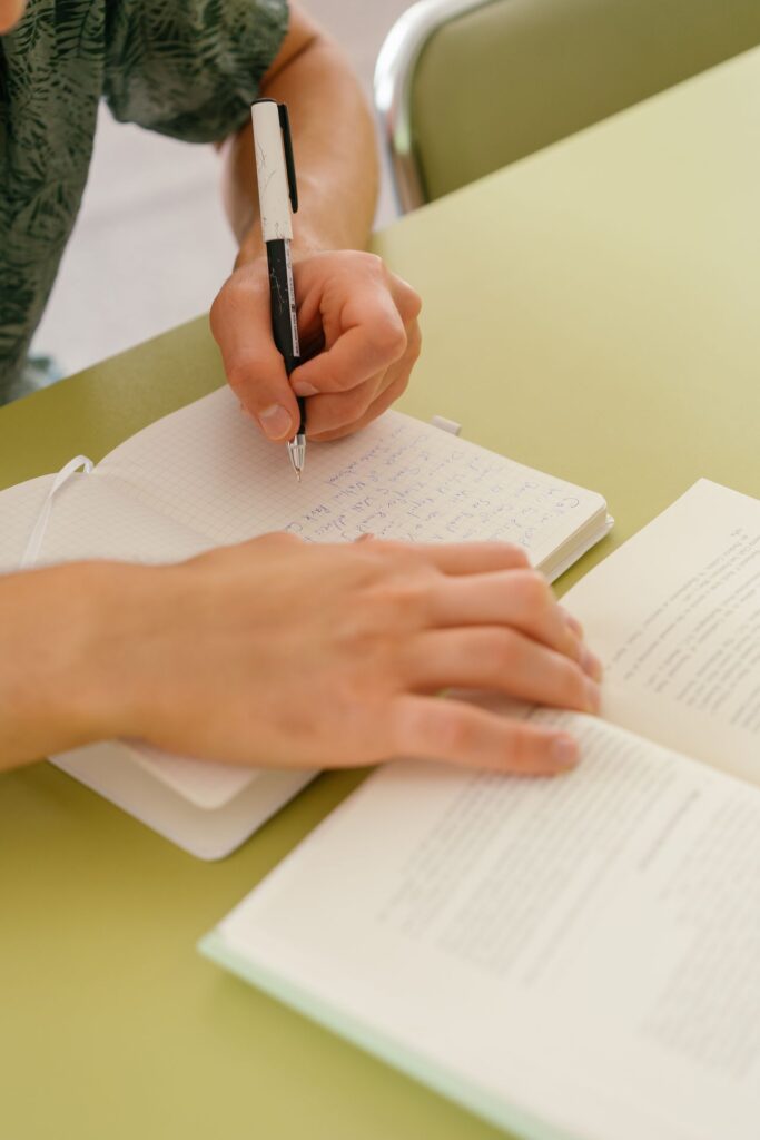 SEND_Paperwork_Images - Northants Send Family Guidance Close-up of a hand writing in a grid notebook with a black-and-white pen on a pale green table.