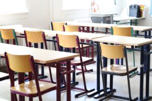 SEND_School_Image - Northants Send Family Guidance Empty classroom with wooden desks and colorful chairs arranged in rows, bright sunlight from windows at the back.